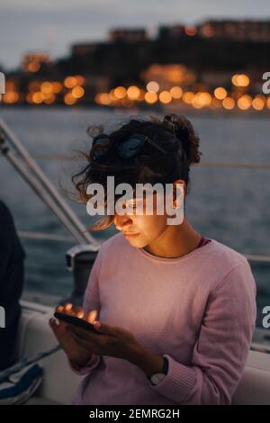 Mid adult woman using smart phone while sitting in boat during sunset Stock Photo