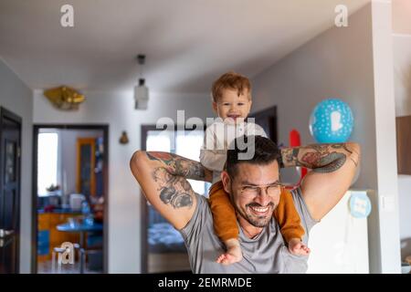 Happy father carrying son on shoulder while standing at home Stock Photo