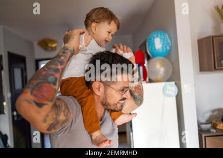 Happy father carrying son on shoulder while standing at home