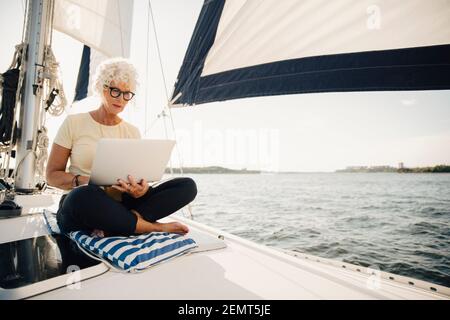 Senior woman working remotely while sailing boat on sunny day Stock Photo