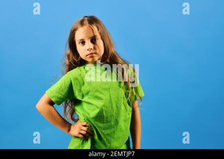 Kid poses as Bgirl in cool style. Child looks like hip hop star wearing casual clothes. Girl with confident face on blue background. Childhood and lifestyle concept. Stock Photo