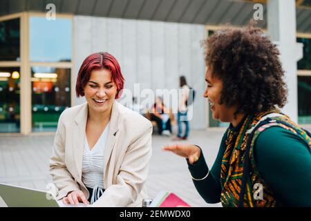 Female students laughing while studying together in university campus Stock Photo