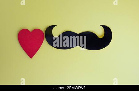 Father's Day concept. Black mustache and red heart on a yellow paper background Stock Photo