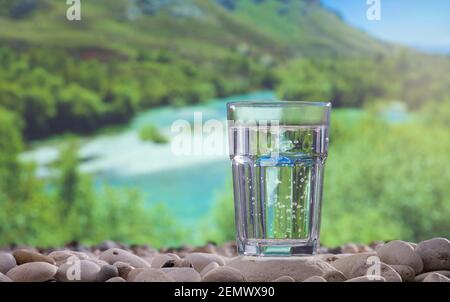 Glass of water on stones and river in background Stock Photo
