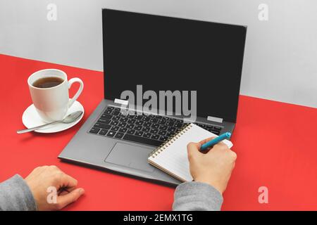 Mockup blank back screen laptop and office supplies on the desk, man is using notepad, a cup of tea on a flat lay background photo Stock Photo