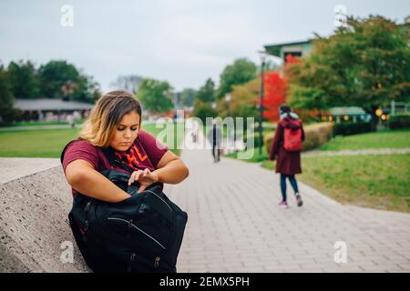 Female student peeking in backpack while standing in college campus Stock Photo