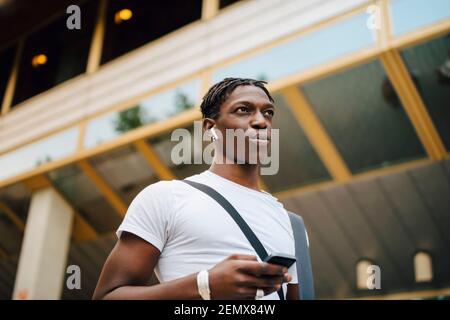 Young male student listening music through wireless in-ear headphones in university campus Stock Photo