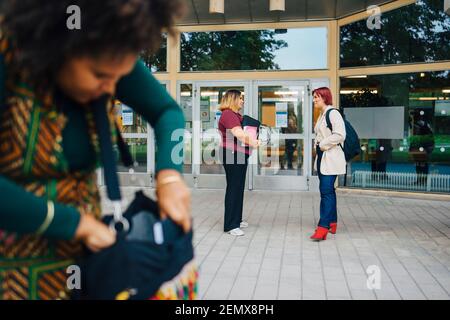 Female students talking with each other while standing at university campus Stock Photo