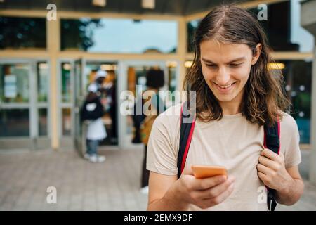 Smiling male student using mobile phone in university Stock Photo
