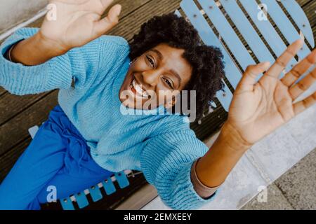 High angle portrait of smiling woman sitting on deck chair in balcony Stock Photo