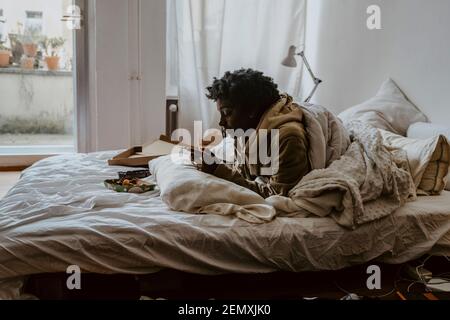 Young woman using smart phone while lying on bed at home Stock Photo