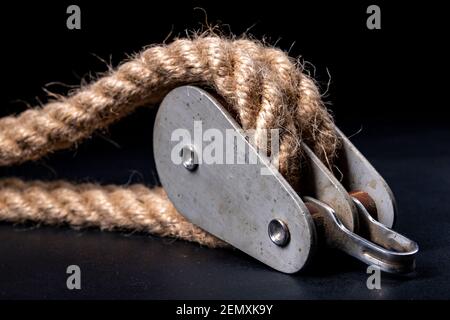 Thick jute rope wrapped on rollers in a sailing pulley. Accessories used on yachts for sailing in the sea. Dark background. Stock Photo