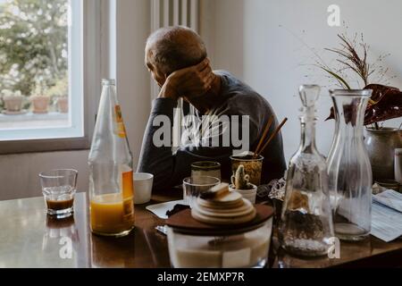 Senior man with hand behind head looking through window in living room Stock Photo