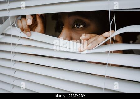 Depressed woman looking through window blinds Stock Photo