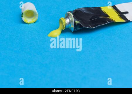 Tube of spilling yellow acrylic paint on art paper background Stock Photo