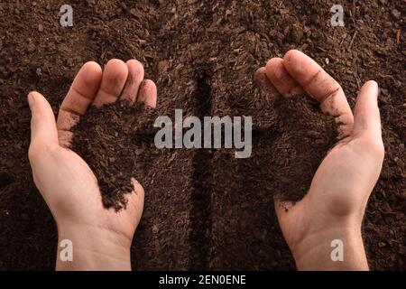 Hands with earth and cross engraved in the center on the earth floor. Horizontal composition. Top view. Stock Photo