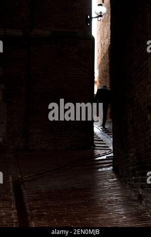 In Urbino, Italy, an elderly person walks with difficulty through the narrow uphill alleys Stock Photo