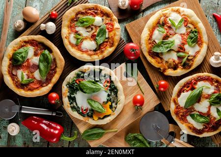 Whole fresh pizzas with green basil, tomatoes, mushrooms and egg on old painted wood Stock Photo
