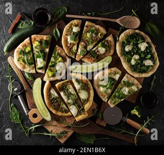 Cutted green pizzas on dark background with green vegetables and greens overhead view Stock Photo