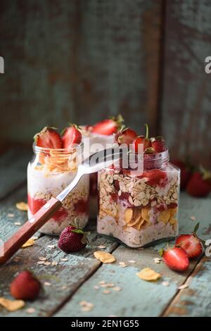 Healthy summer breakfast. Overnight oats with strawberry and cornflakes in glass jars on shabby blue background copyspace vertical Stock Photo