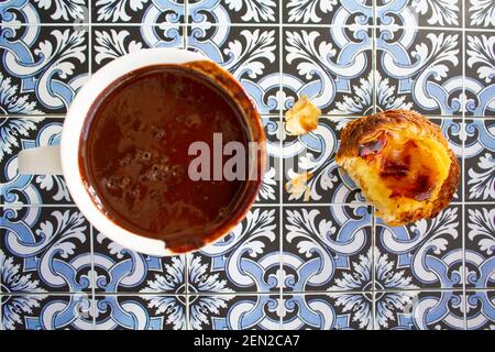 Top viwe of cup with hot chocolate and custard tart called pastel de nata on portuguese tiles background Stock Photo