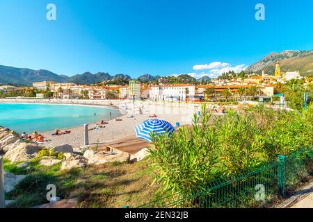 Tourists and locals enjoy a sunny day on the French Riviera as they relax on the sandy Plage de Fossan Mediterranean beach in Menton, France Stock Photo