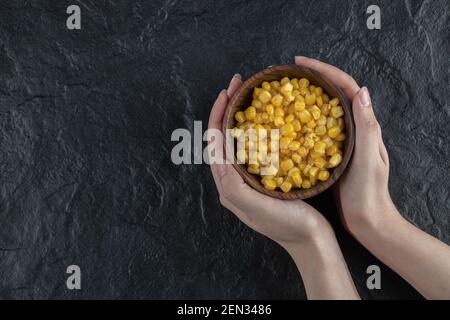 Female holding Canned sweet corn in bowl over black background Stock Photo