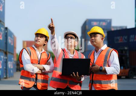 Asian foreman holding laptop and explaining the various operations in the container depot terminal to worker. Stock Photo