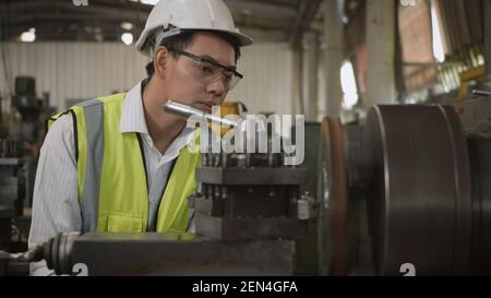 Asian professional mechanical engineer or operation man wear uniform goggles safety working on workshop metal lathe industrial manufacturing factory, Stock Photo