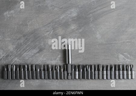 Screwdriver bits for various slots laid out in a row on a gray concrete surface. Stock Photo