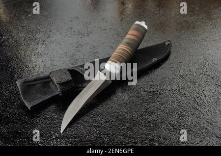 Elegant hunting knife in a sheath with a leather handle on a black textured background. Selective focus. Stock Photo