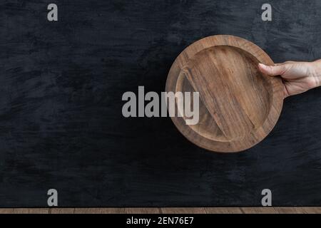 Holding a wooden platter in the hand on black background Stock Photo