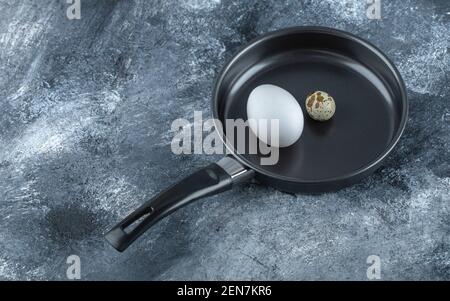Fresh organic chicken and quail eggs in black frying pan Stock Photo