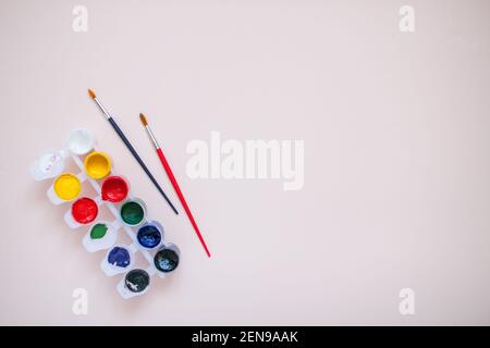 Bright paints and two brushes on a light pink background. Preparation for drawing Stock Photo