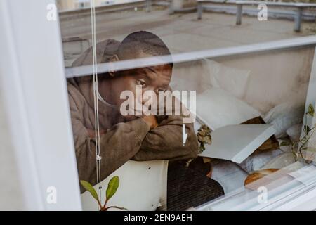 Depressed man sitting at home seen through window Stock Photo