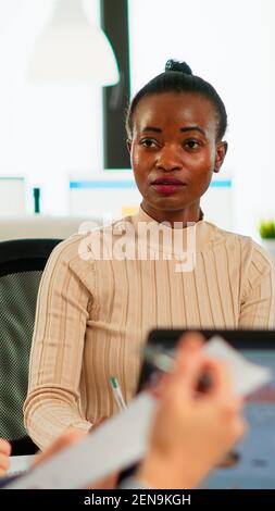 Confident african leader negotiating with business group explaining contract benefits at formal board meeting consulting corporate clients presenting commercial offer sitting at conference office table Stock Photo