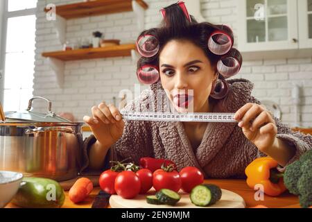 Funny crazy woman looking at tape measure while cooking healthy food in the kitchen Stock Photo