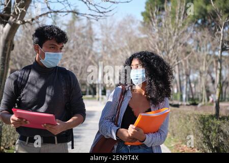 Two latin students wearing face mask and holding folders. New normal in the university campus. Stock Photo