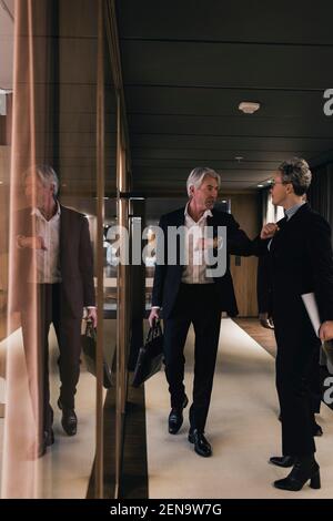 Senior businessman greeting mature businesswoman while giving fist bump in office corridor Stock Photo