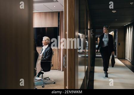 Full length of businesswoman walking in corridor while looking at board room Stock Photo