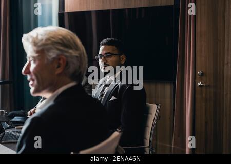 Confident businessman sitting with senior male colleague in board room during meeting Stock Photo