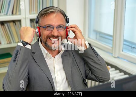 Successful Mature Businessman Sitting at Office Desk Raising Hand in Yes Gesture, Celebrating Business Success. Smiling Excited Businessman Gesturing. Stock Photo