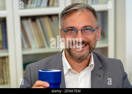 Middle Aged Businessman Sitting at Office Desk During Coffee Break. Portrait of Mature Man With Cup of Coffee. Stock Photo