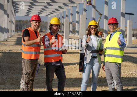 Group of Business People in Hardhats With Thumbs Up on Construction Site. Project Management and Field Crew Meeting on Construction Site. Stock Photo