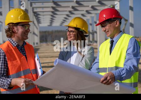 Group of Mixed Business People in Yellow and Red Hardhats Discuss a Project on Site Under Construction. Business, Building, Teamwork  Concept. Stock Photo