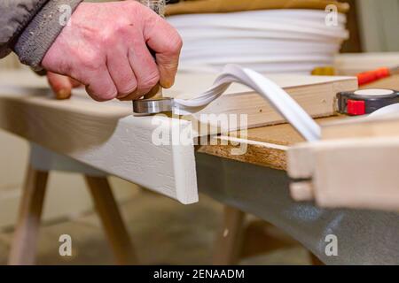 A carpentry worker uses improvised hand tool and puts a rubber for sealing on the wooden door frame. Stock Photo