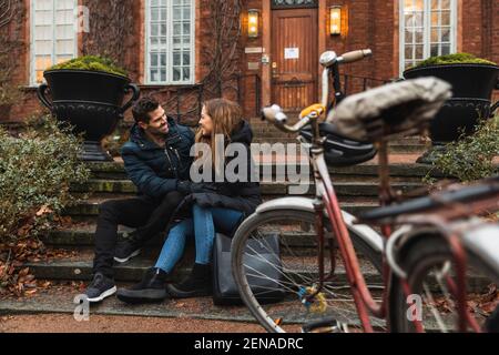 Smiling couple looking at each other while sitting on steps against house Stock Photo
