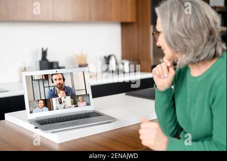 Smiling entrepreneur, aged woman sitting at the laptop, home, meeting with the business partners to sum up the results of the cooperation, in different parts of the world, distance is not a hindrance Stock Photo