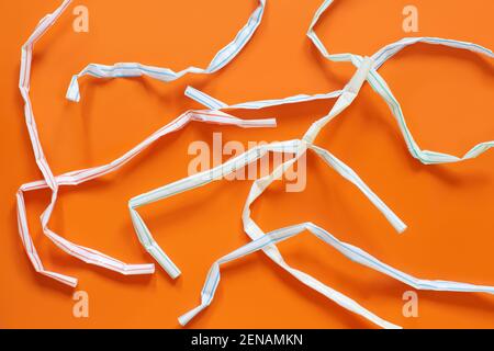 Used plastic drinking straws on the orange background top view. Single-use plastic problem Stock Photo