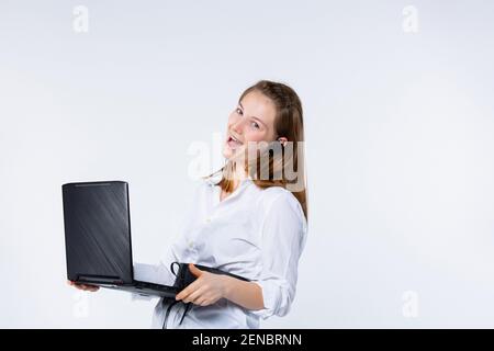 Caucasian blonde woman smiling, holding laptop computer, looking to camera, excited for success on light gray background. Young and confident Stock Photo